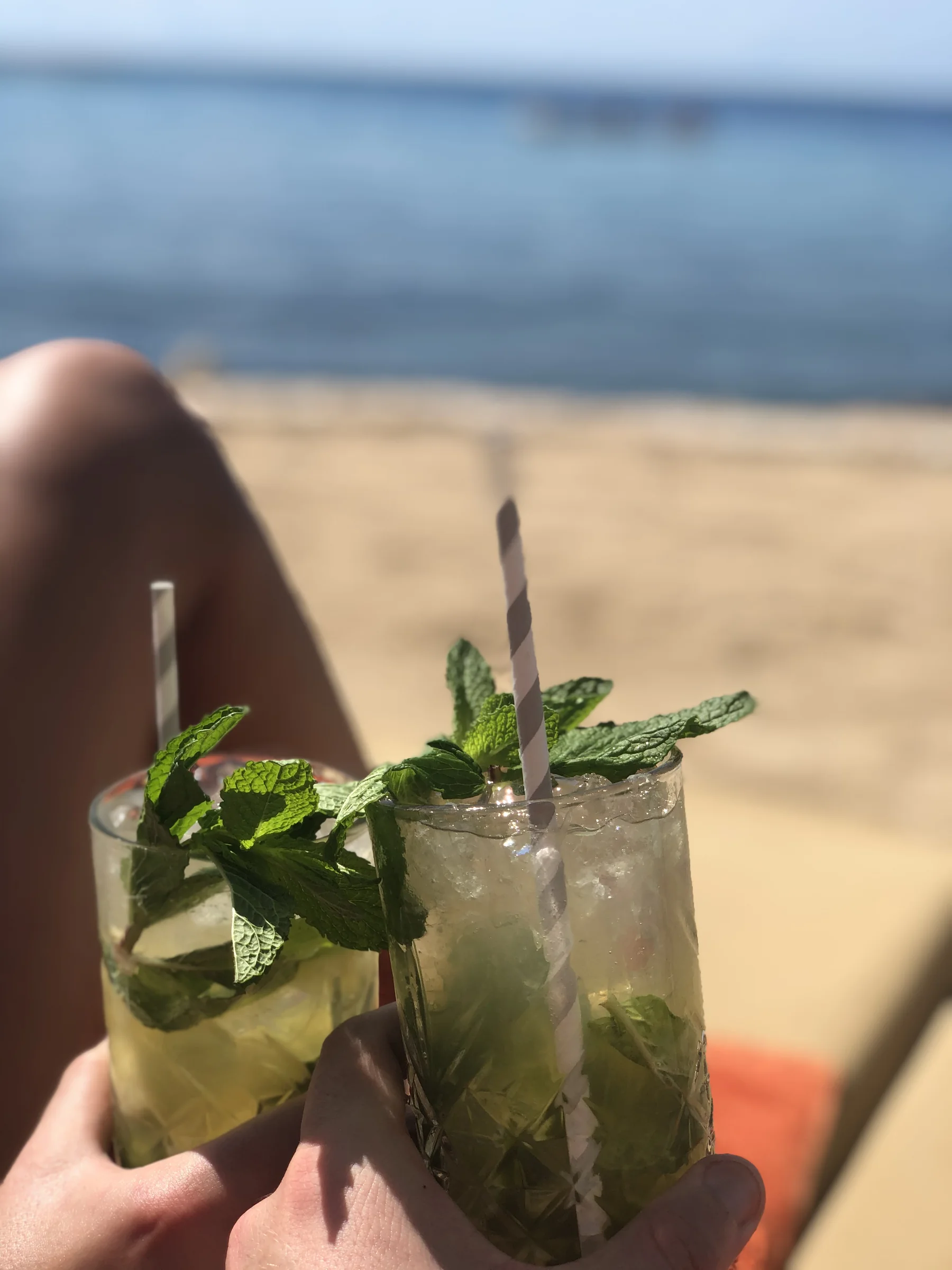 Cocktail in de hand met strand en palmbomen op de achtergrond