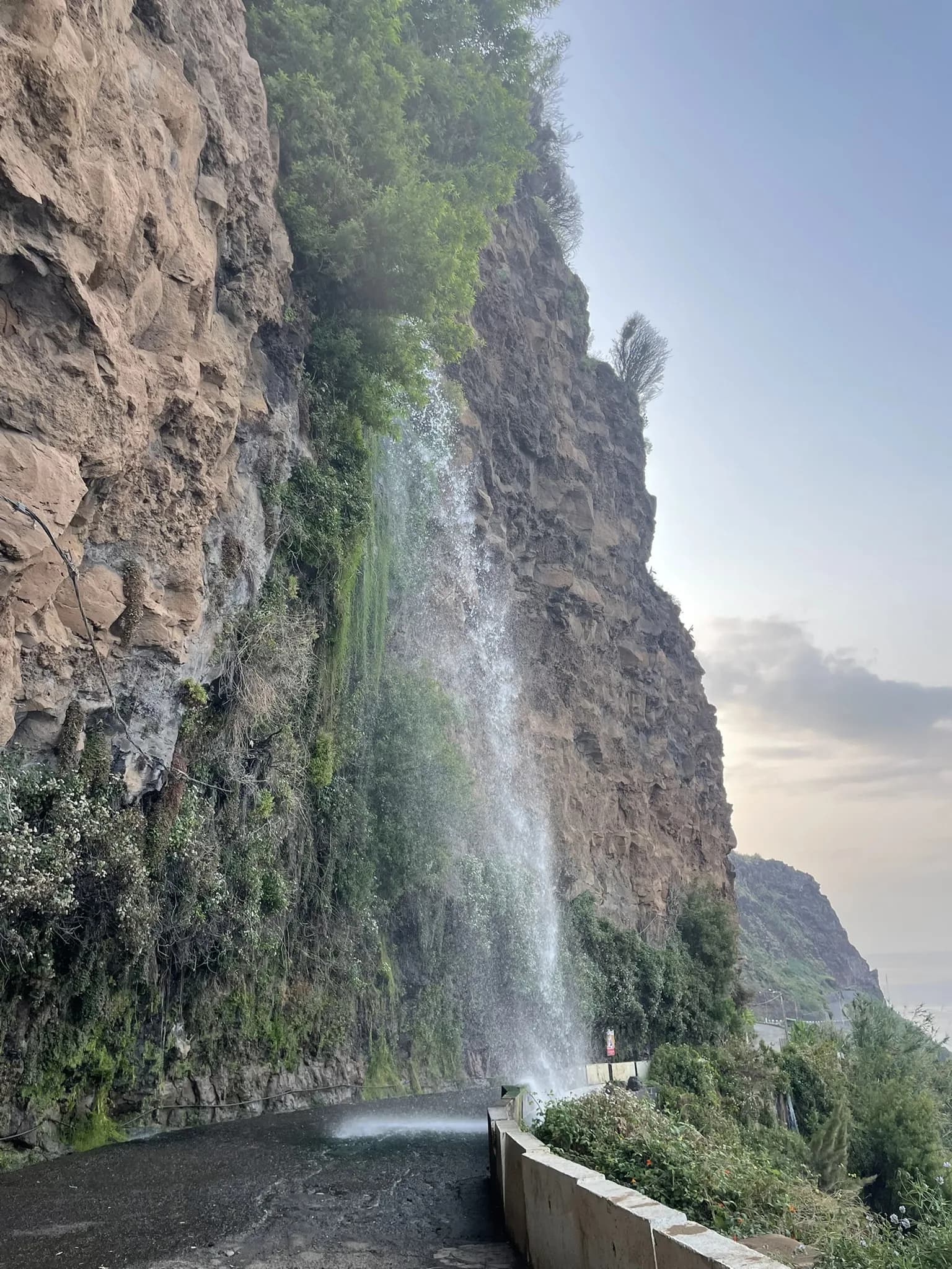 Cascata dos Anjos stroomt over de oude kustweg langs de rotswand