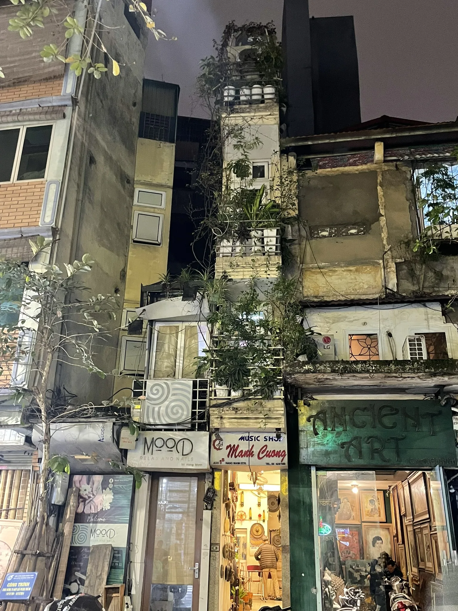 Smalle woningen en winkelgevels in Hanoi bij avond